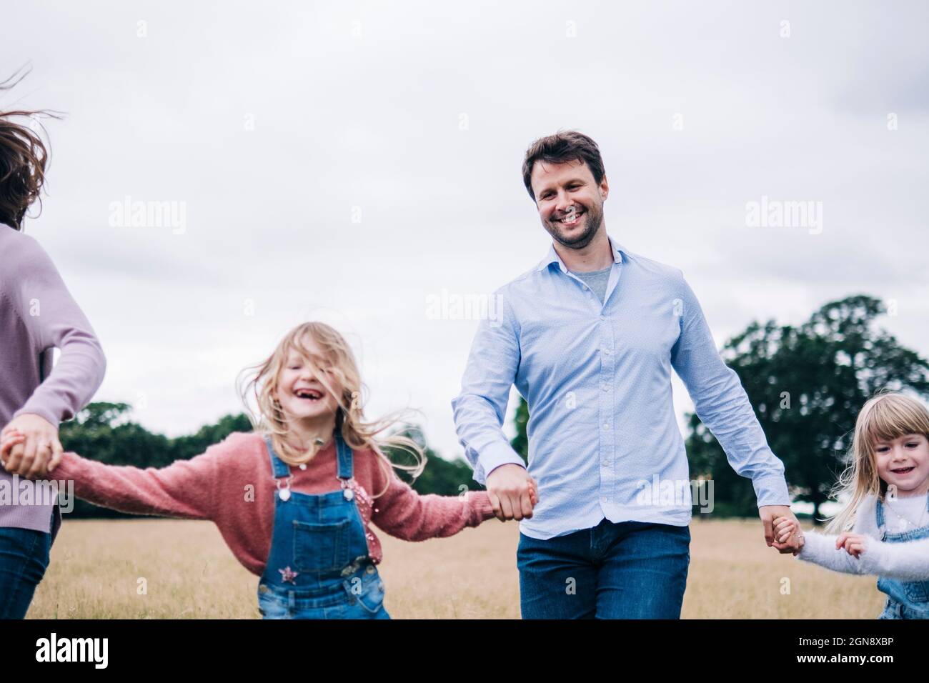 Man and woman holding hands of girls while running on meadow Stock Photo