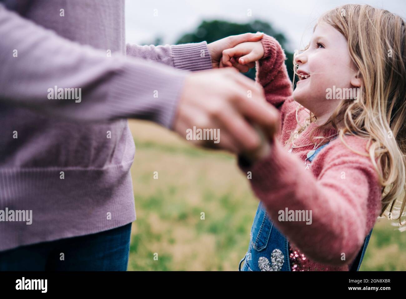 Smiling daughter holding hands of mother while playing outdoors Stock Photo