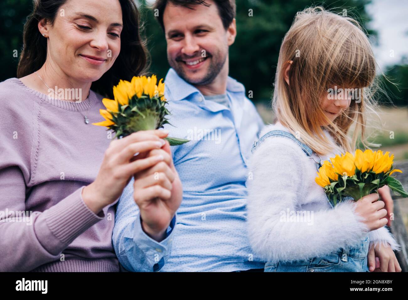 Woman and girl holding sunflower while sitting with man at park Stock Photo