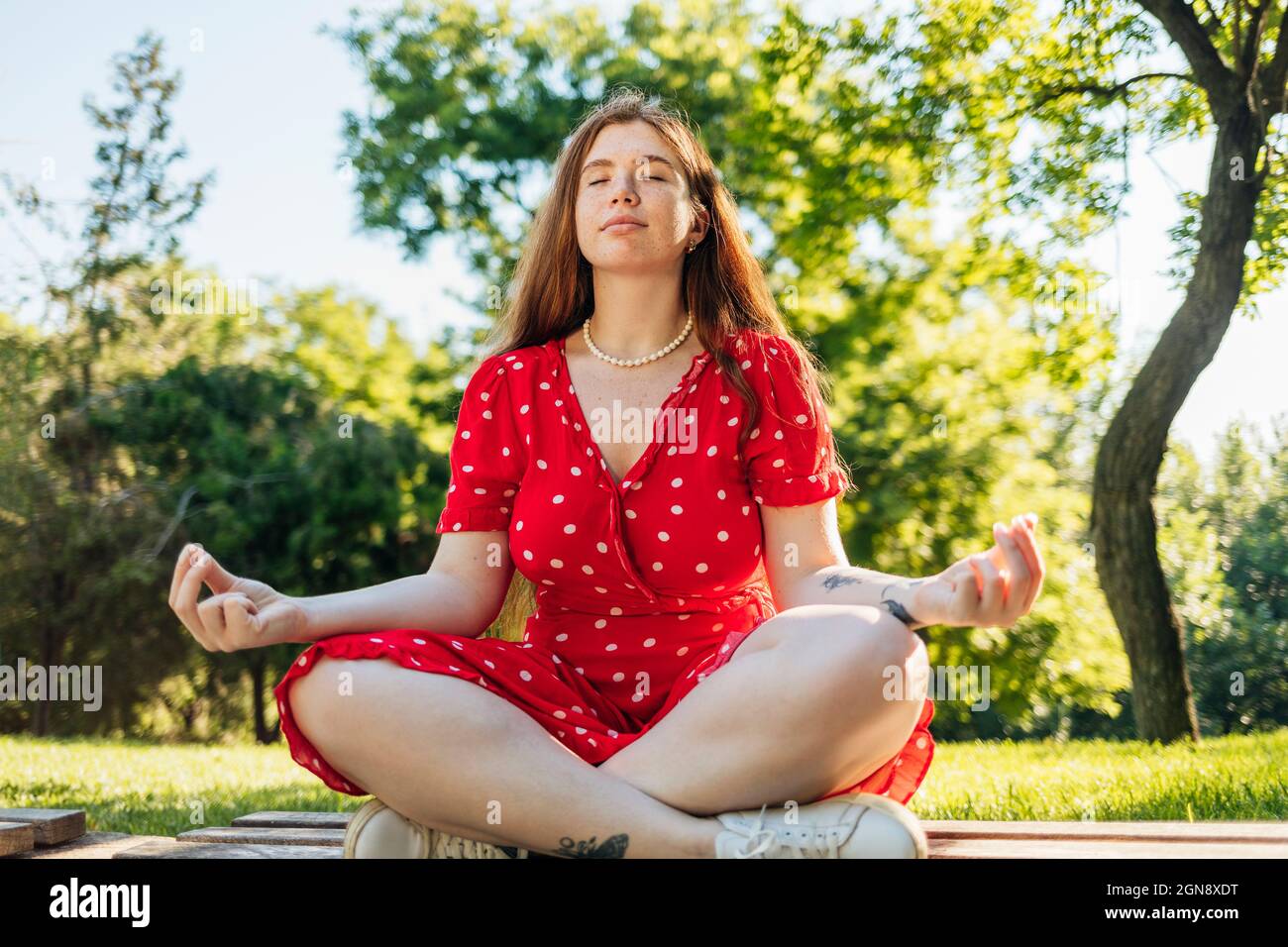 Woman practicing yoga while sitting cross-legged at park Stock Photo