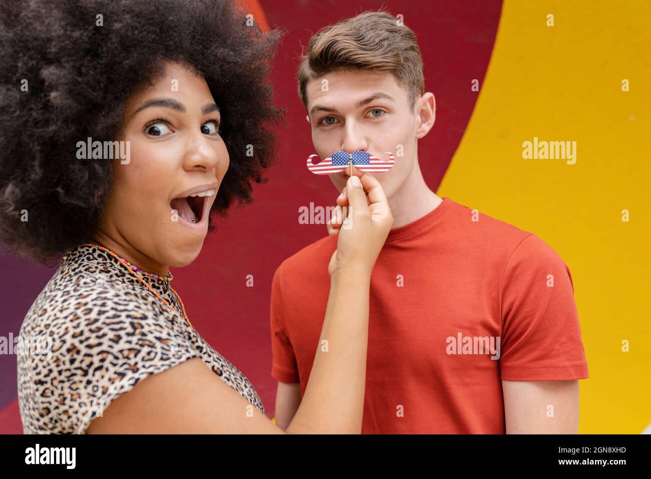 Surprised woman holding mustache prop over man's face Stock Photo