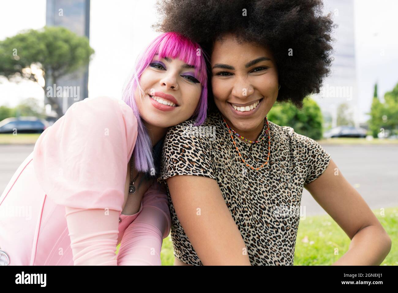 Woman with dyed hair leaning on Afro female friend at park Stock Photo