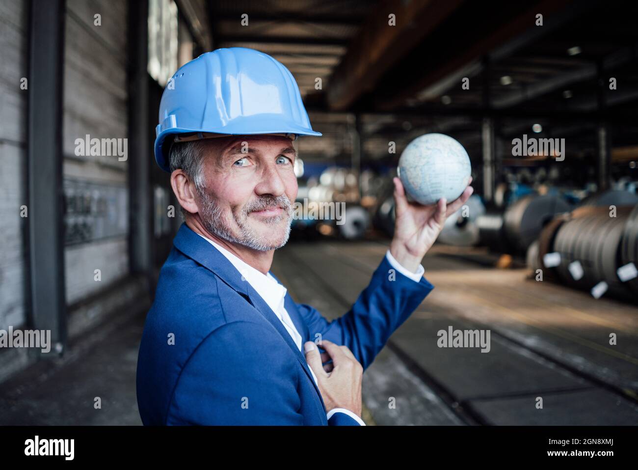 Male engineer with hardhat holding globe at warehouse Stock Photo