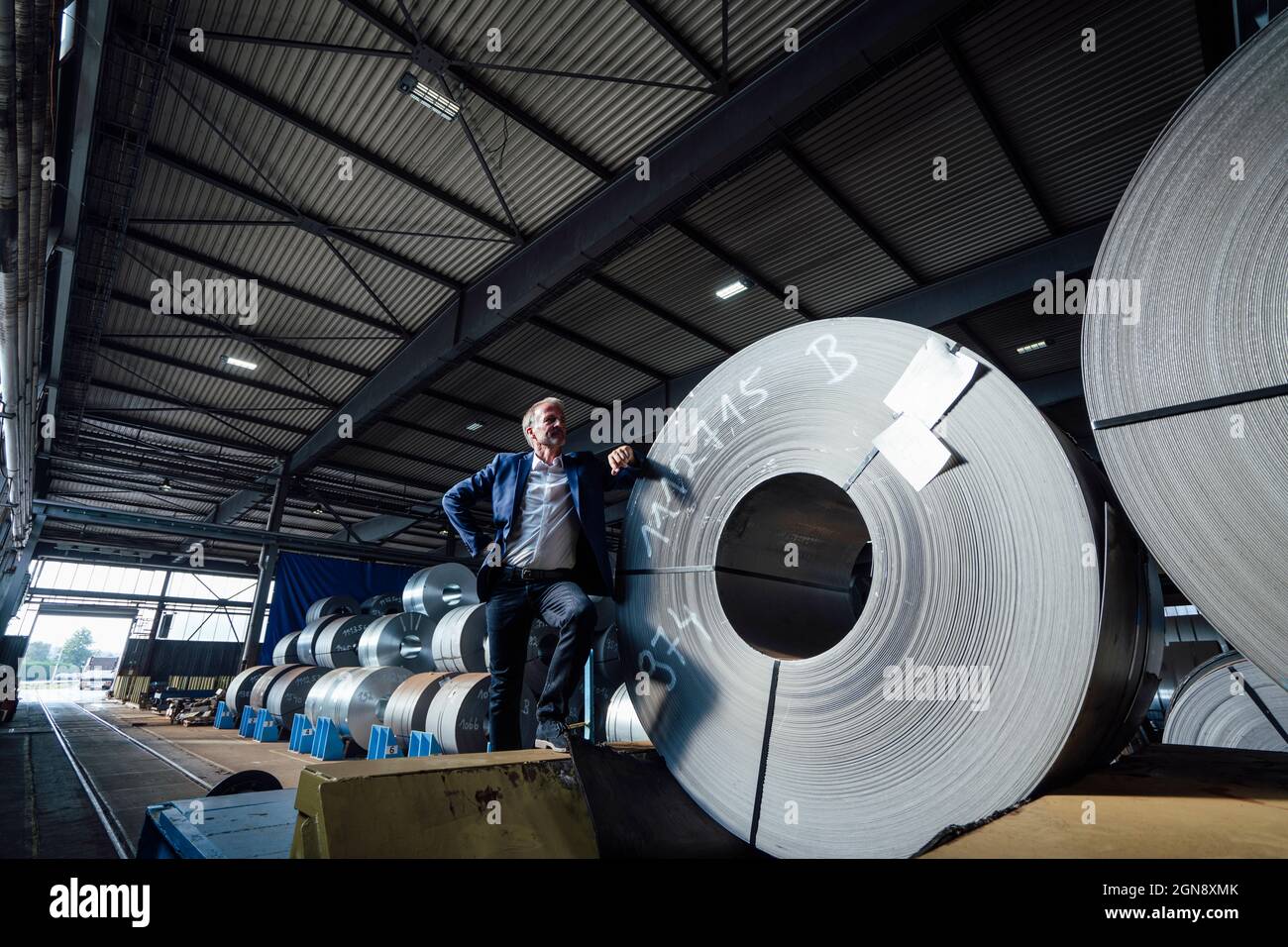 Businessman leaning on rolled up metal sheet at distribution warehouse Stock Photo