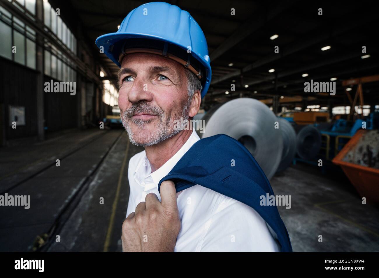 Male engineer with hardhat holding blazer while looking away Stock Photo