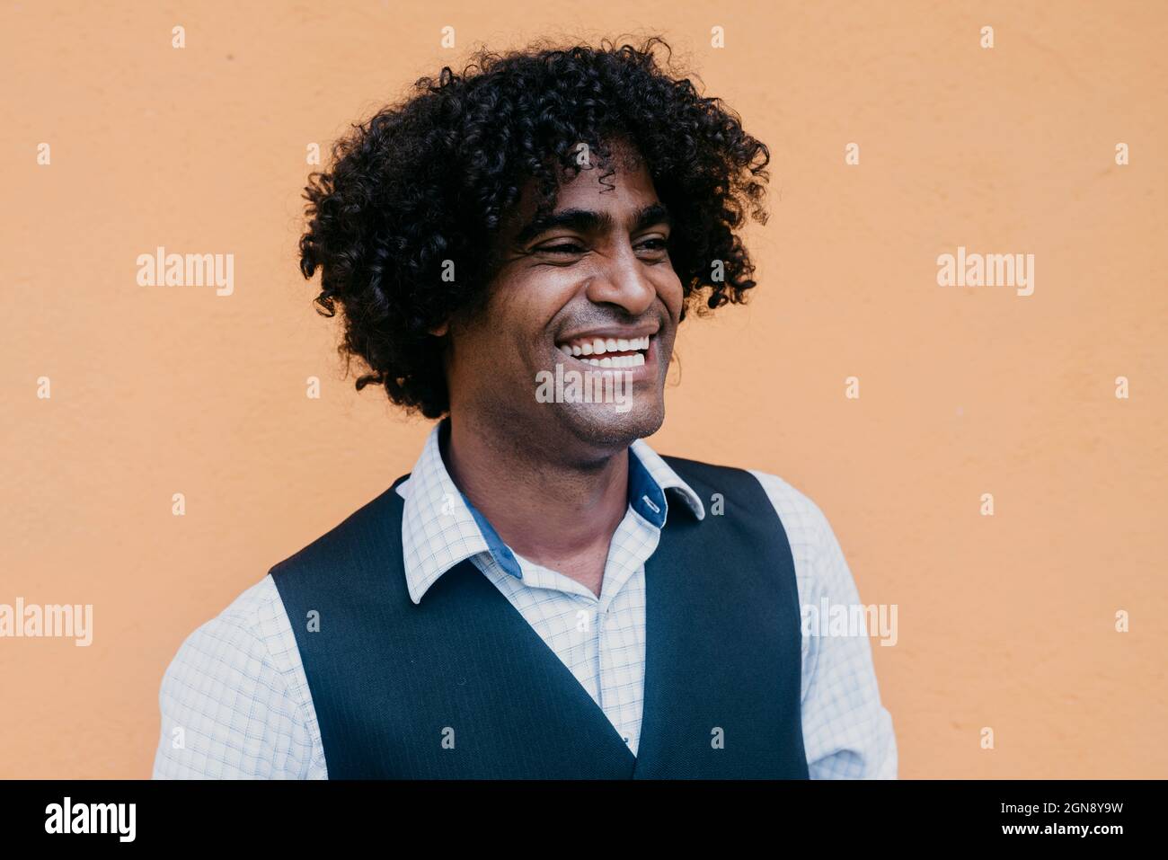Cheerful man with curly black hair in front of beige wall Stock Photo