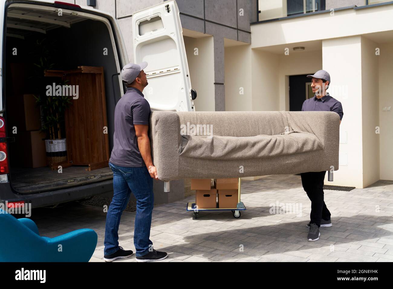Male delivery coworkers unloading sofa from moving van near house Stock Photo