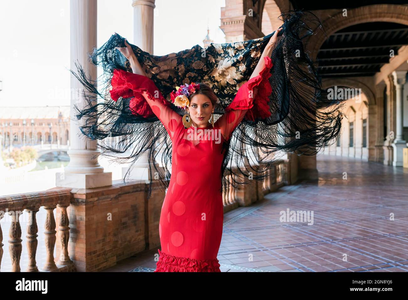 Female flamenco artist holding shawl with hands raised at Plaza De Espana walkway in Seville, Spain Stock Photo
