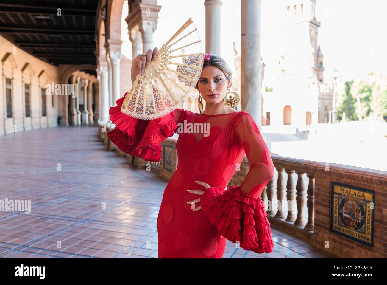 Woman wearing traditional dress holding hand fan at Plaza De Espana walkway in Seville, Spain Stock Photo