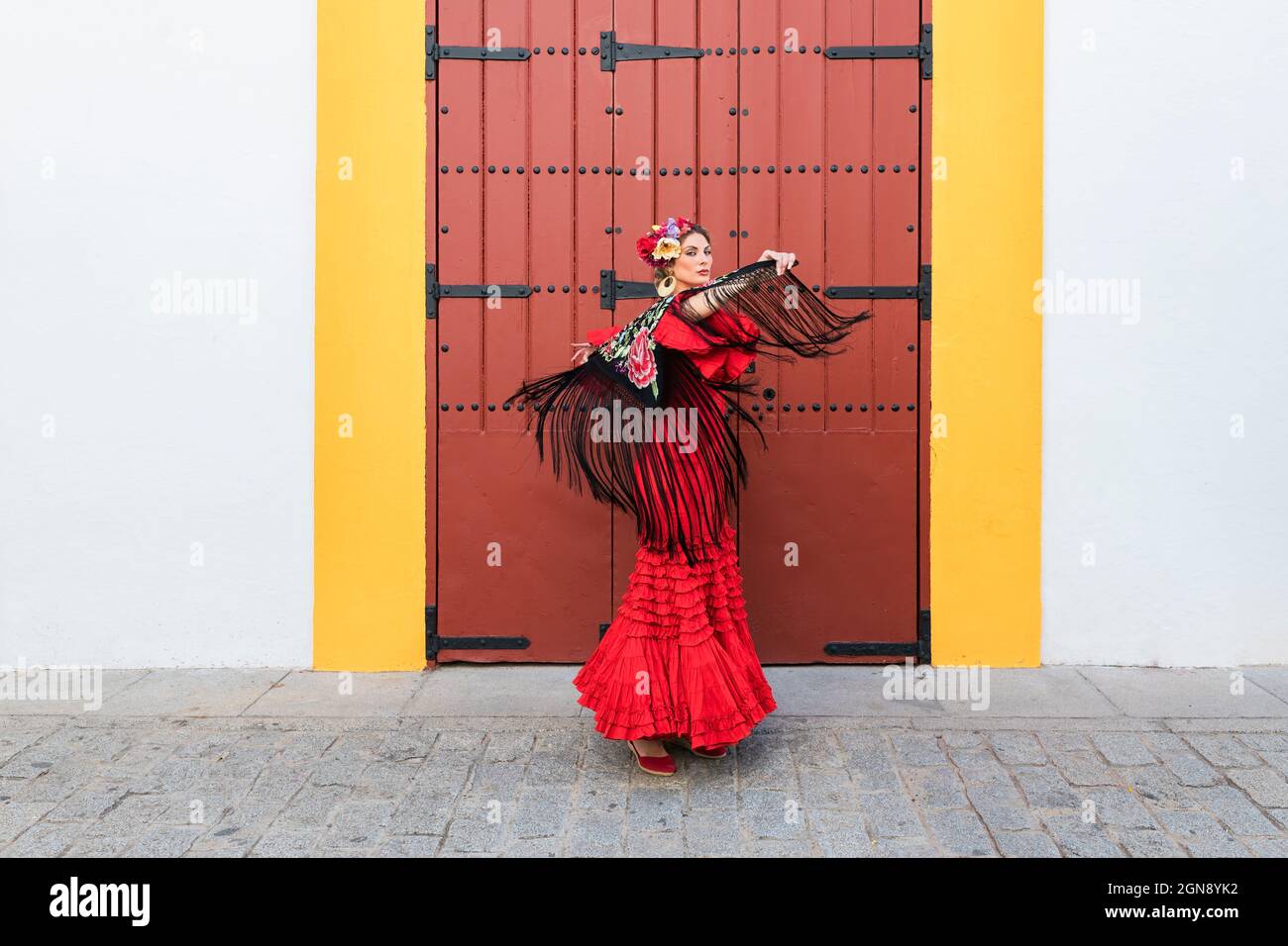 Female artist wearing flamenco dress and shawl dancing on footpath Stock Photo