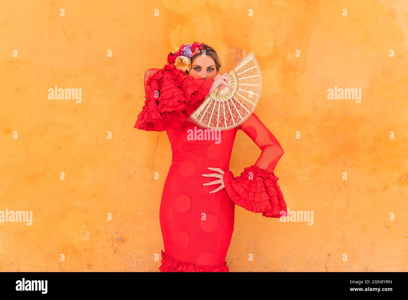 Female dancer wearing red traditional dress standing in front of orange wall Stock Photo