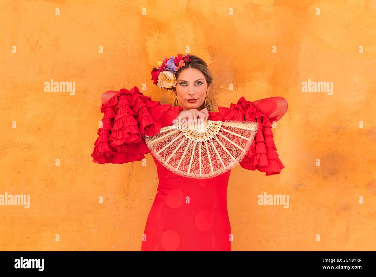 Female flamenco artist holding hand fan while standing in front of orange wall Stock Photo