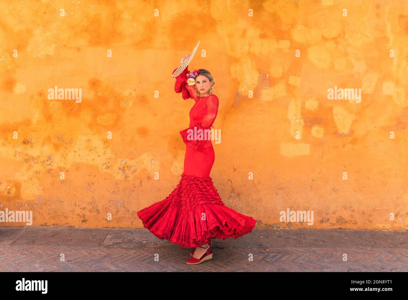 Female flamenco artist with hand fan dancing on footpath Stock Photo