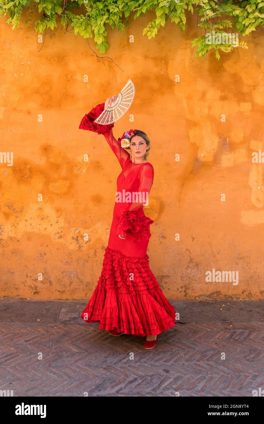 Female dancer with hand fan dancing in front of orange wall Stock Photo