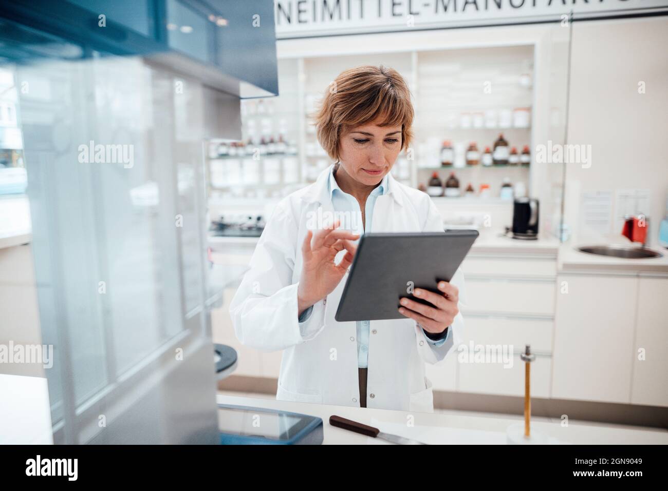 Female pharmacist using digital tablet while standing at laboratory Stock Photo