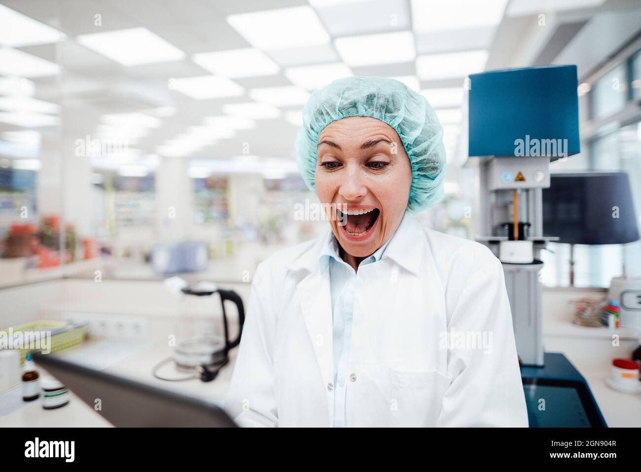 Surprised female pharmacist using digital tablet while standing at laboratory Stock Photo