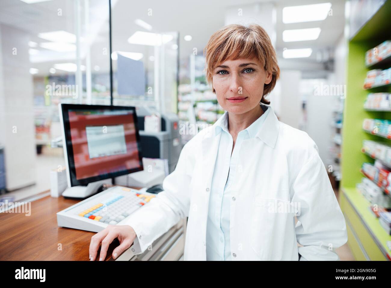 Female pharmacist wearing lab coat standing at checkout counter at