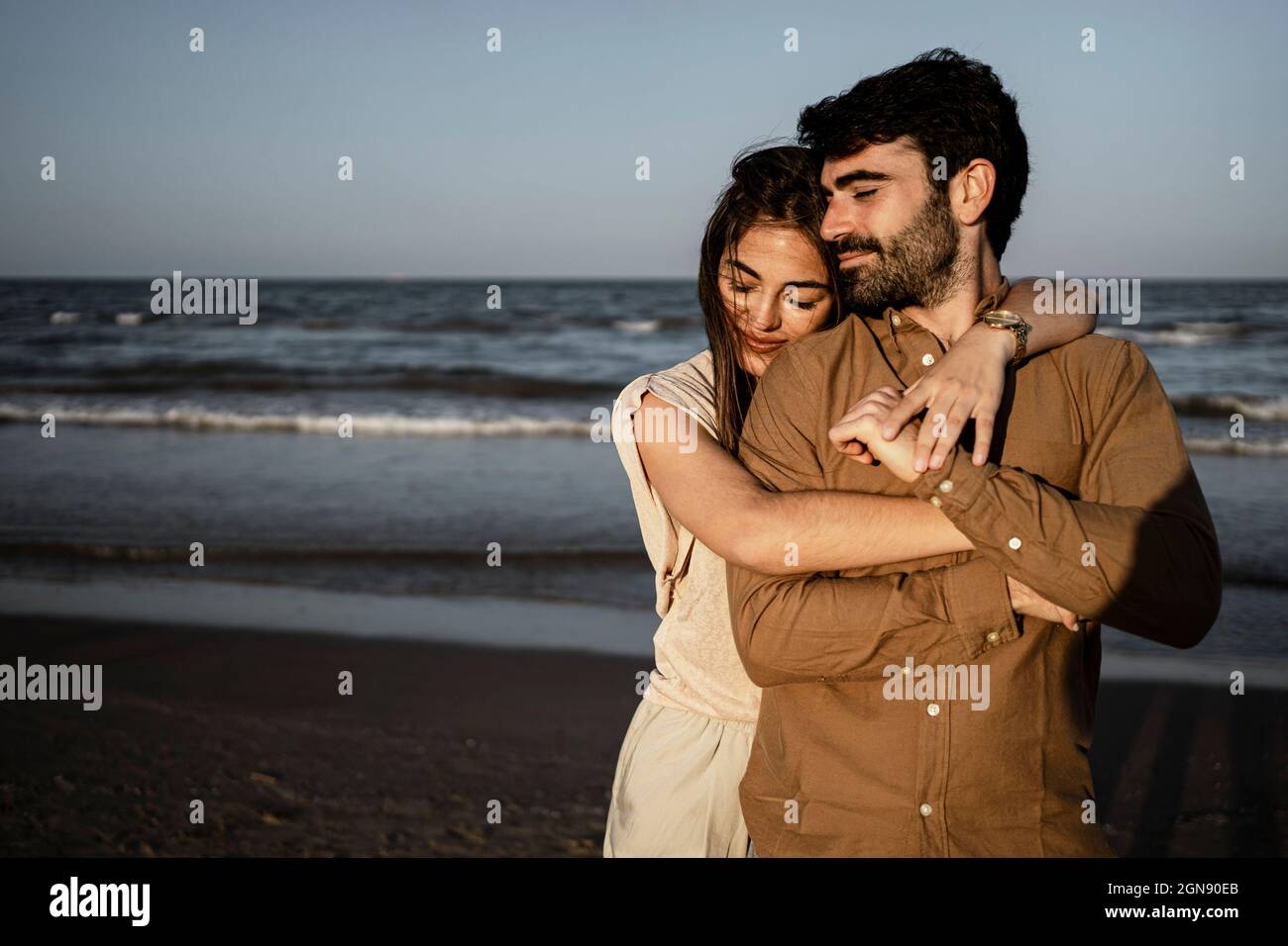 Smiling girlfriend embracing boyfriend from behind at beach Stock Photo