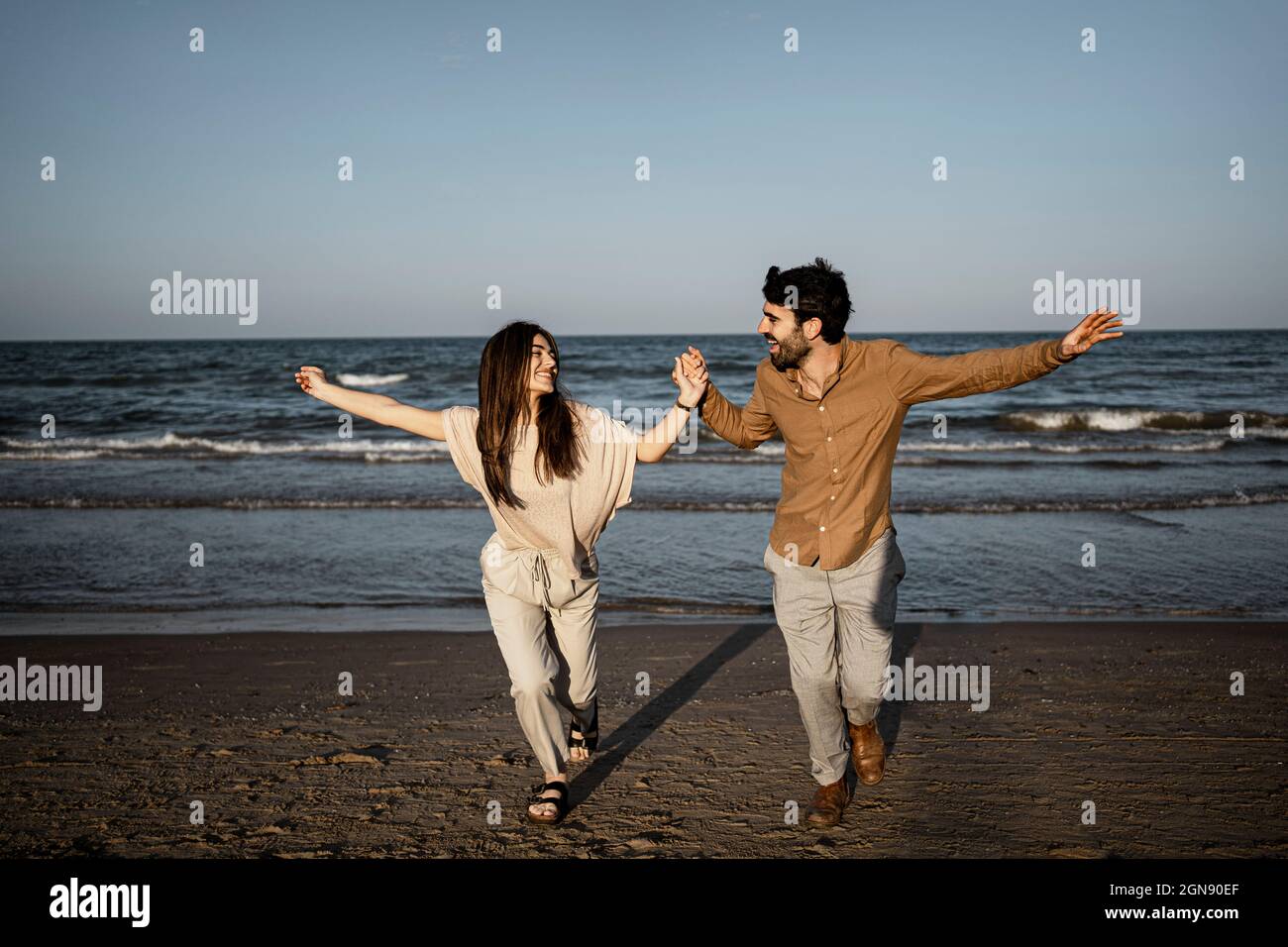 Cheerful couple holding hands while running on beach Stock Photo