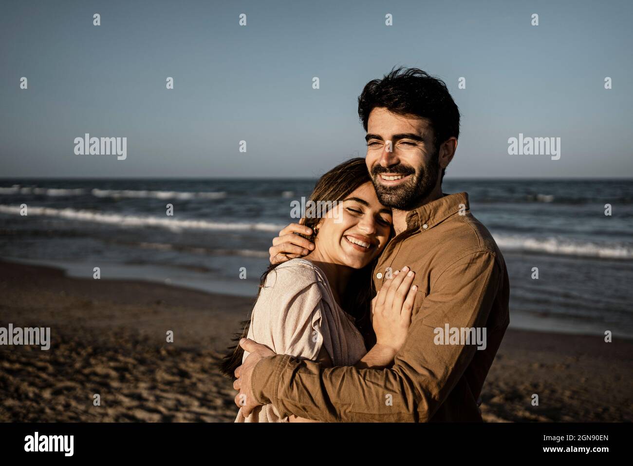 Happy young couple embracing while standing at beach Stock Photo