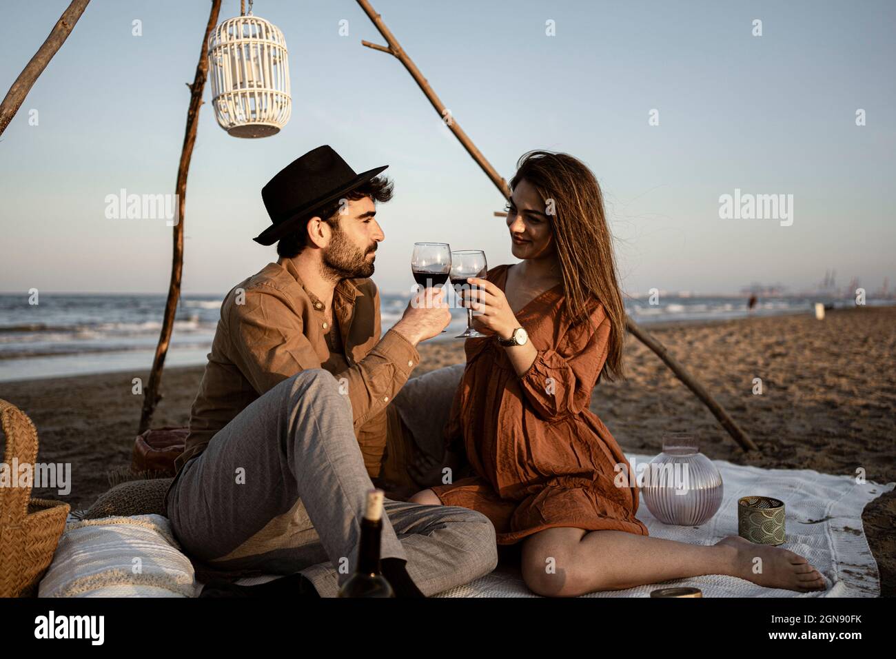 Couple toasting drink while sitting on picnic blanket Stock Photo
