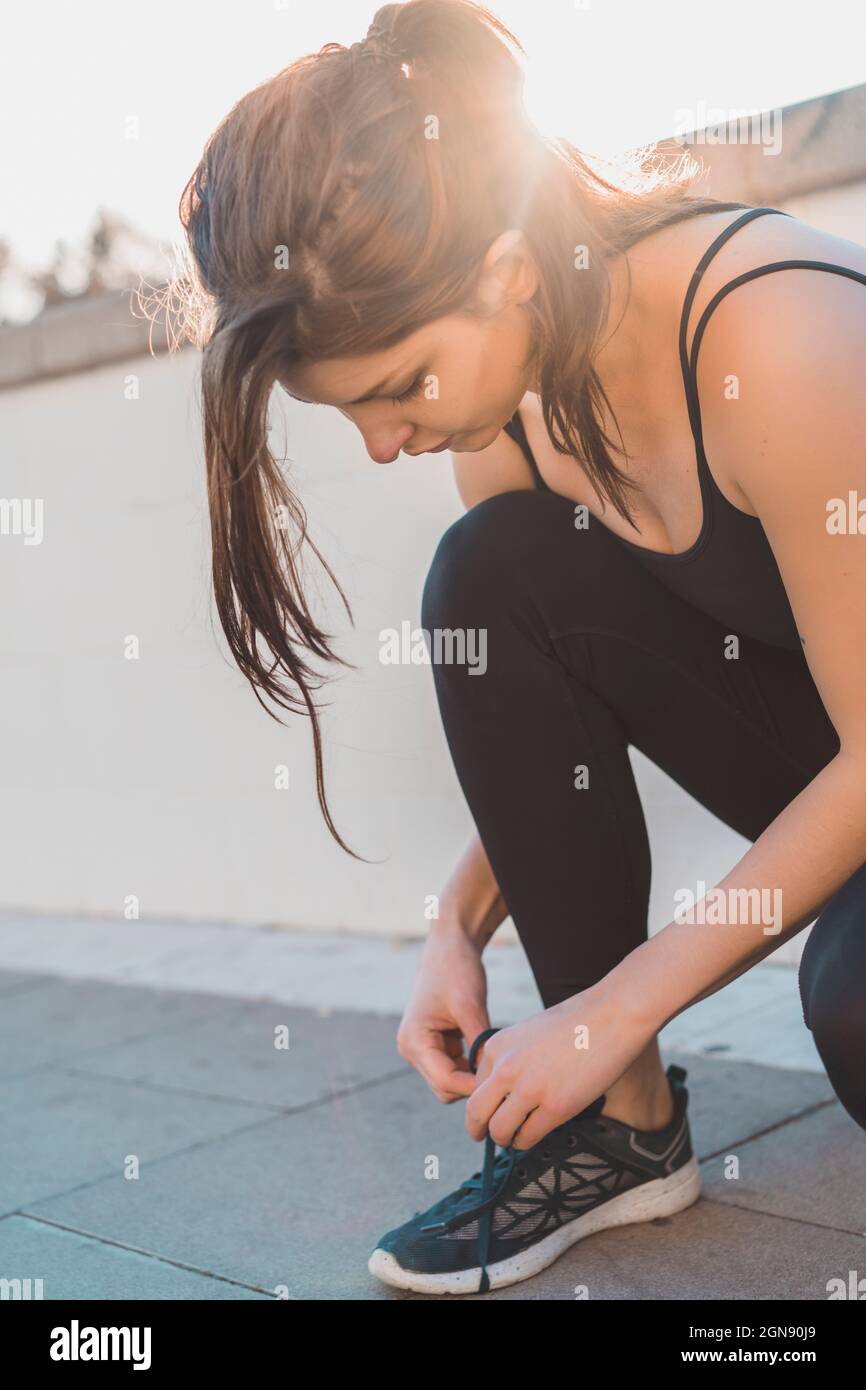 Young woman tying shoelace while crouching on footpath Stock Photo