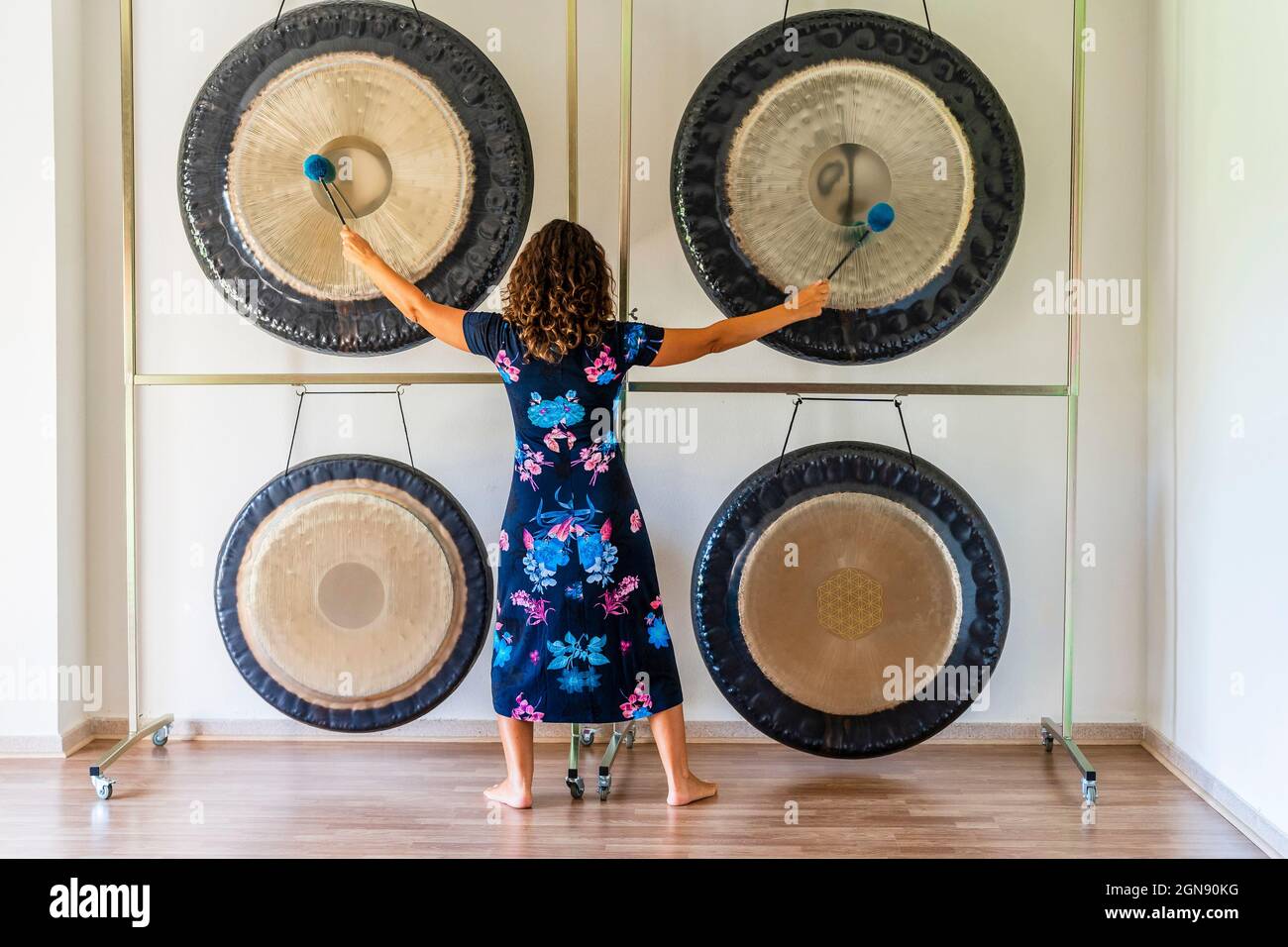 Female sound therapist playing gongs with mallets in studio Stock Photo