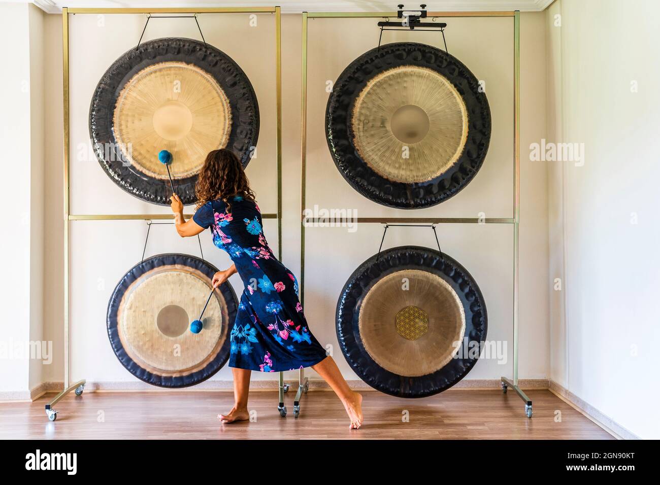 Female sound therapist playing gongs with mallets in studio Stock Photo