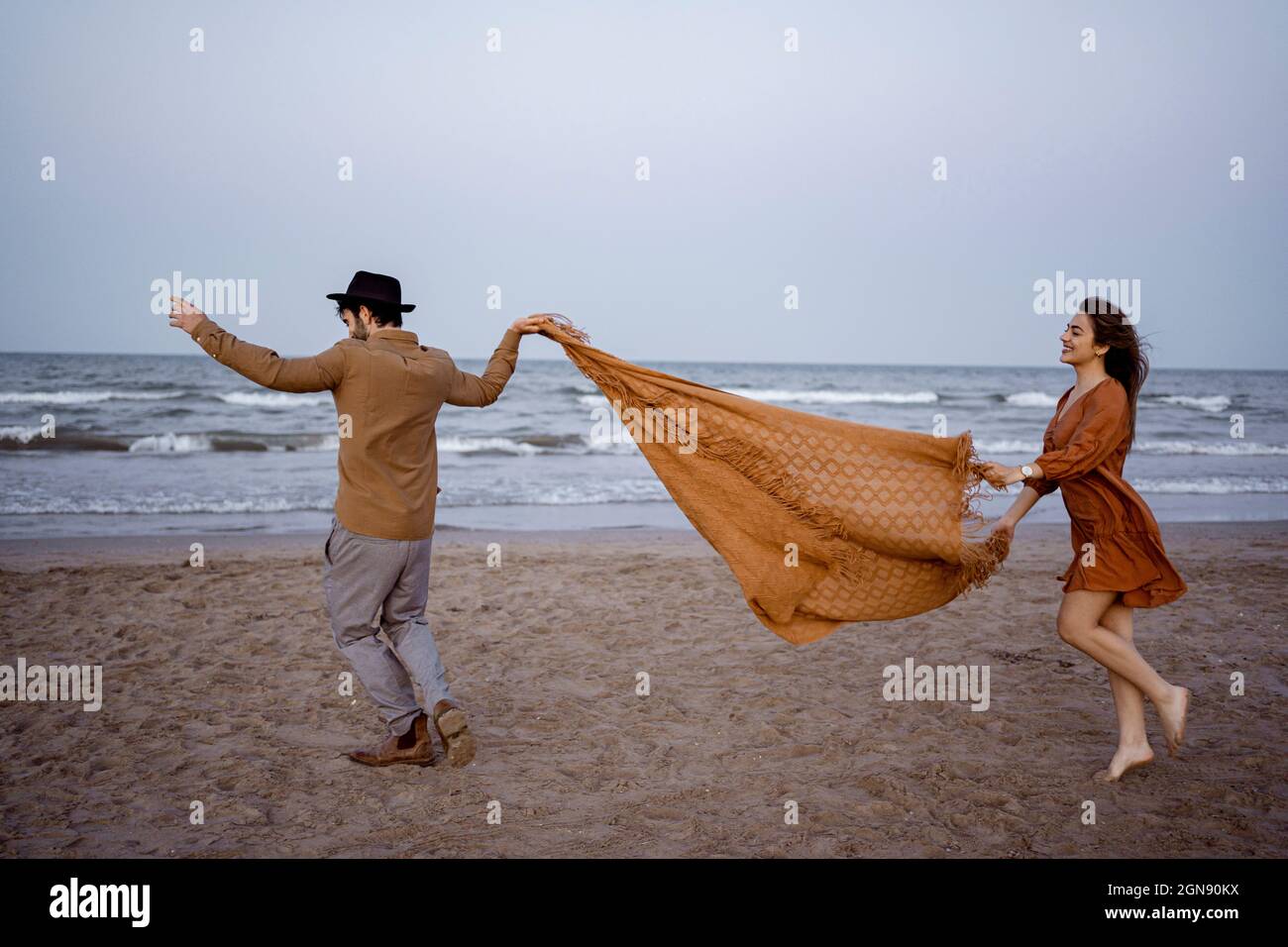 Couple holding blanket while running on beach during sunset Stock Photo