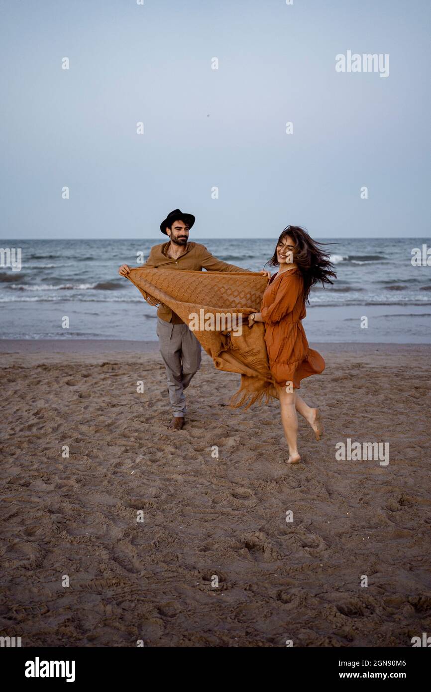 Cheerful couple holding blanket while playing on beach Stock Photo