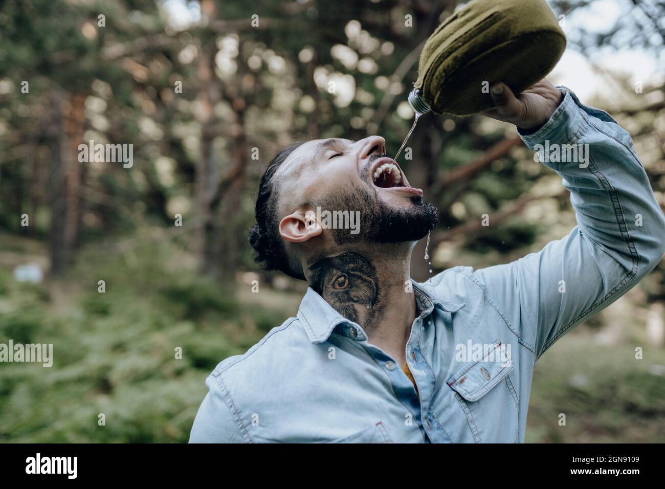 Thirsty bearded male hipster drinking water from bottle in forest Stock Photo