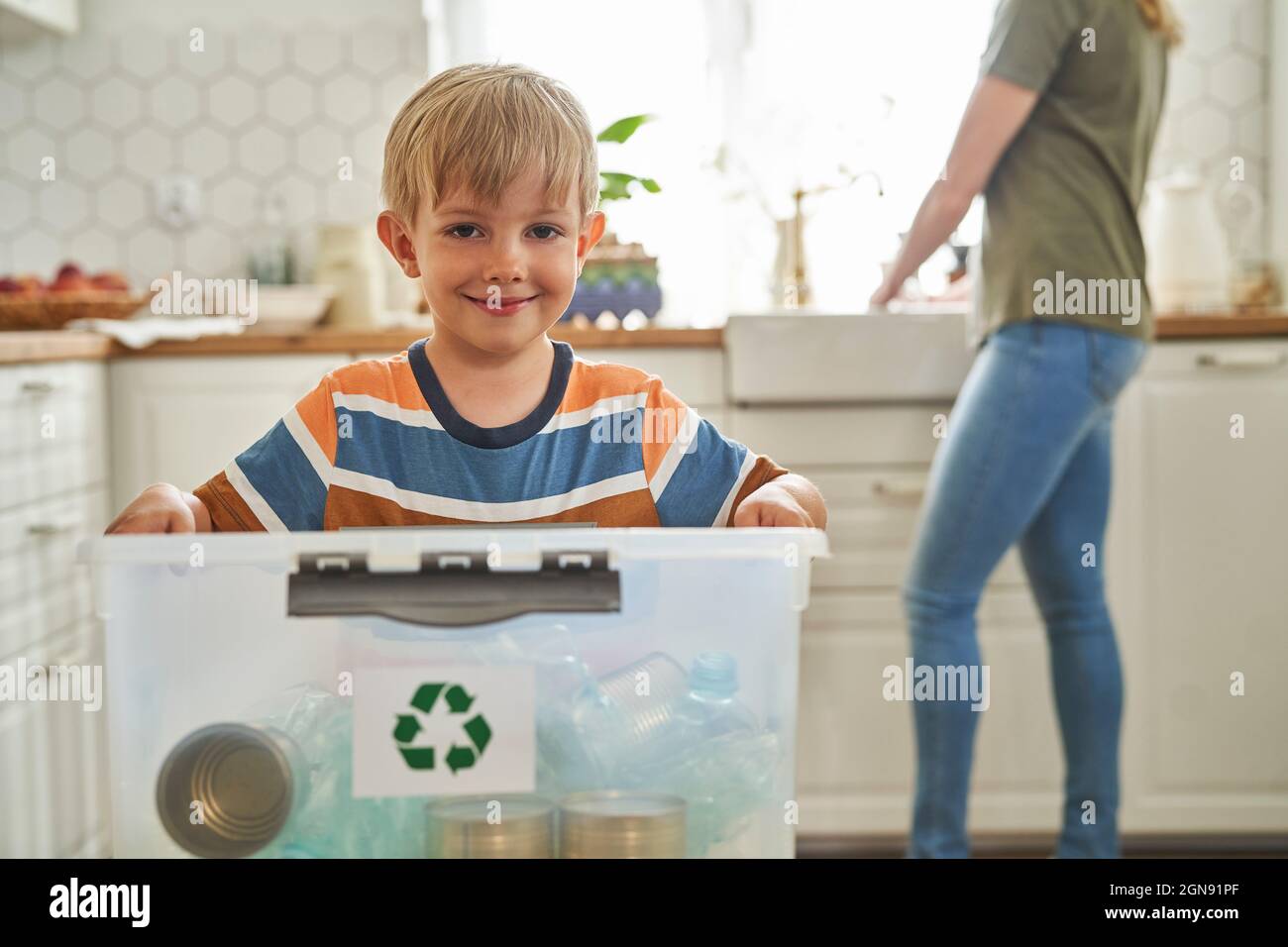 Smiling boy holding recycling container with bottles at home Stock Photo