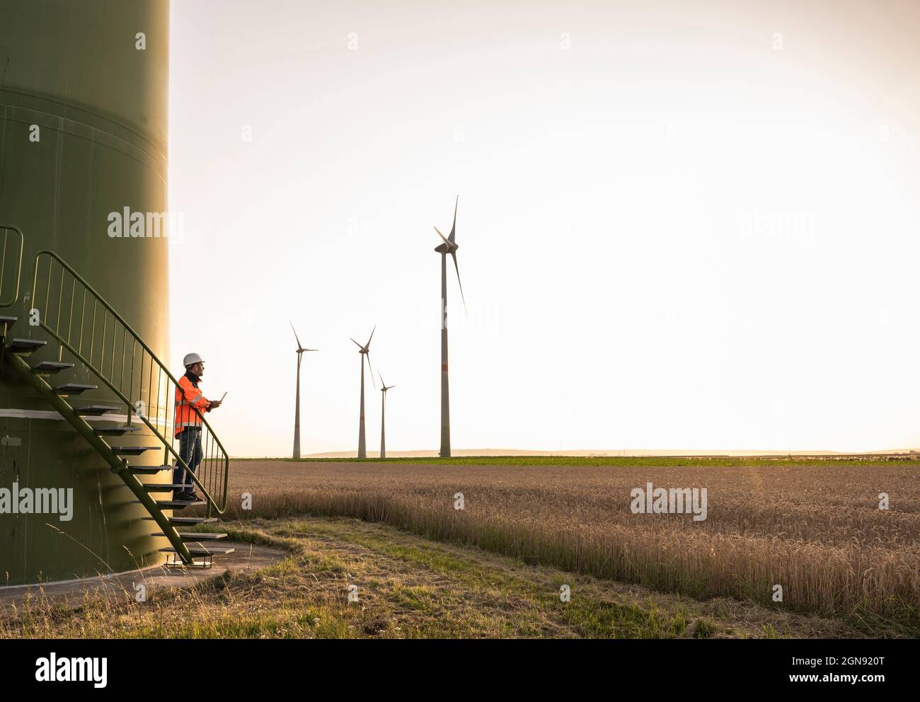 Male technican looking at wind turbine while standing on staircase Stock Photo