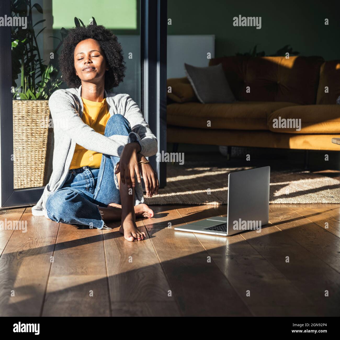Young woman with eyes closed sunbathing in living room Stock Photo