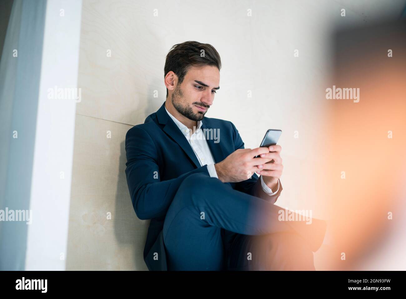 Young businessman text messaging through smart phone while sitting in office Stock Photo