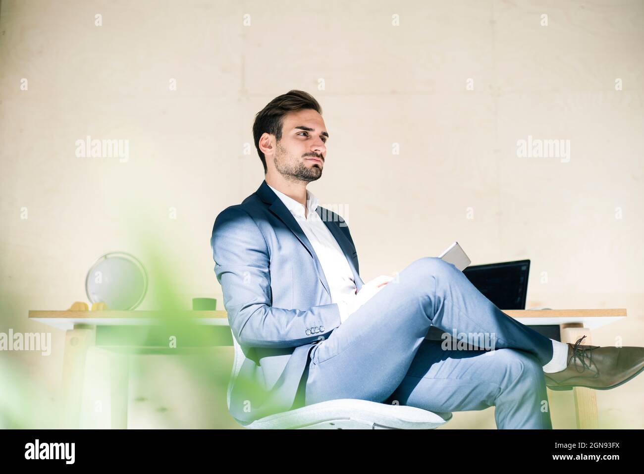 Thoughtful young male professional sitting with digital tablet on chair in office Stock Photo