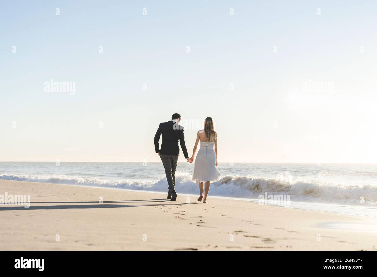 Newlywed couple holding hands while walking on beach Stock Photo