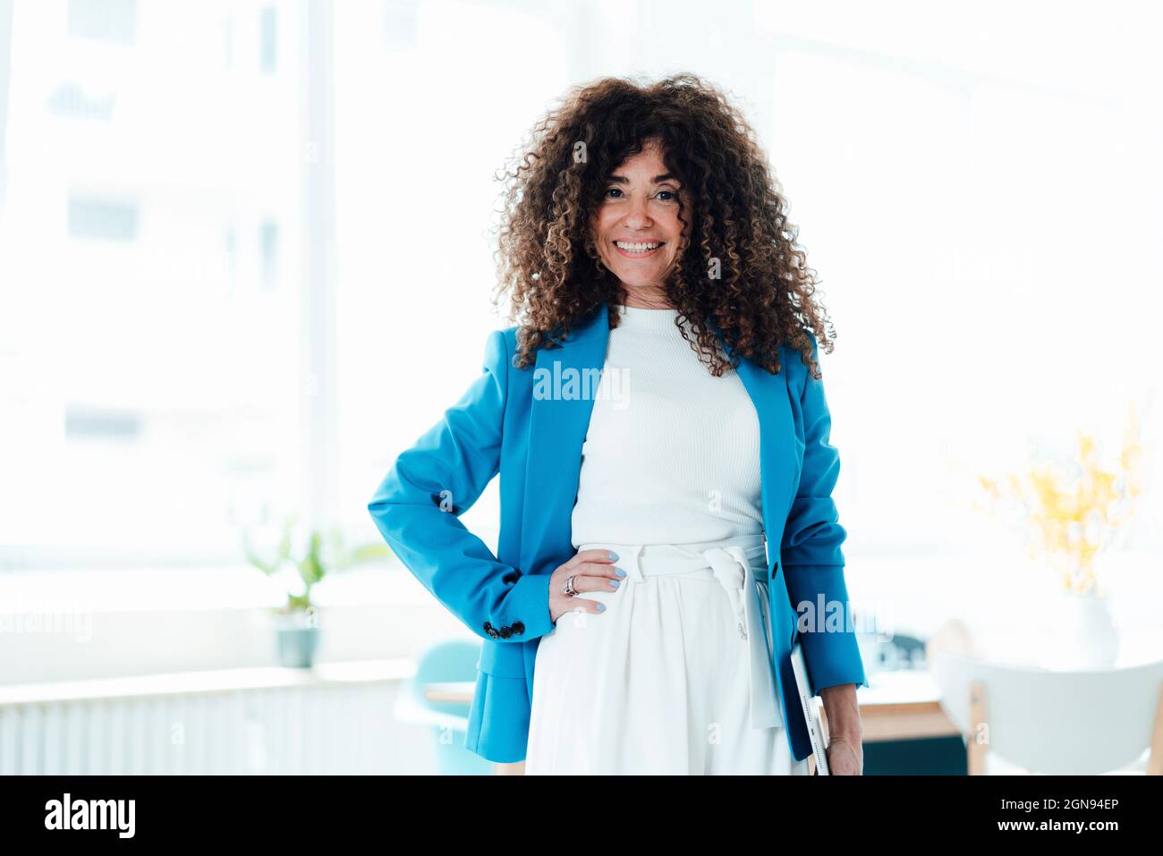 mature-businesswoman-standing-with-hand-on-hip-in-office-stock-photo