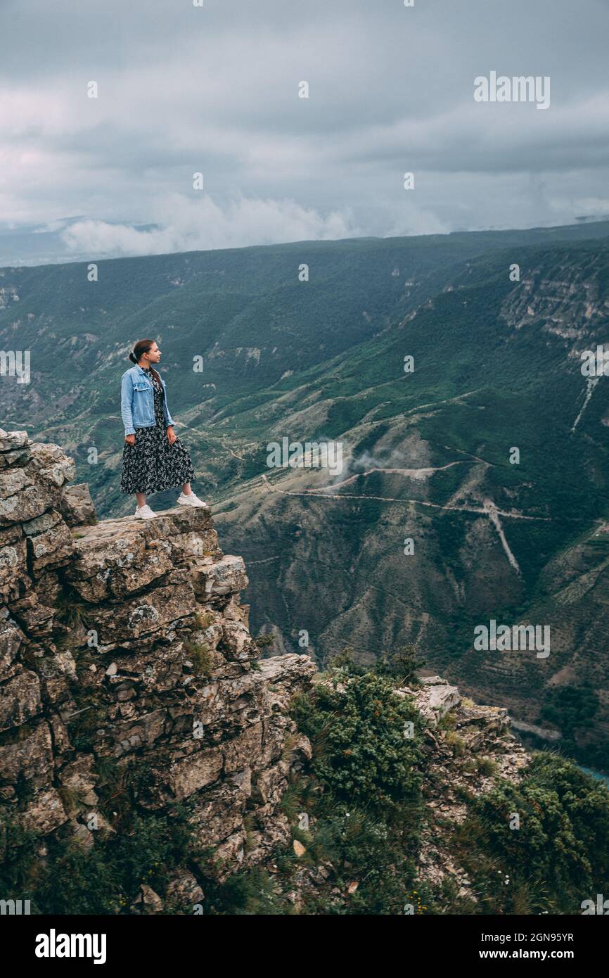 A young traveling woman stands on the edge of a mountain cliff and ...