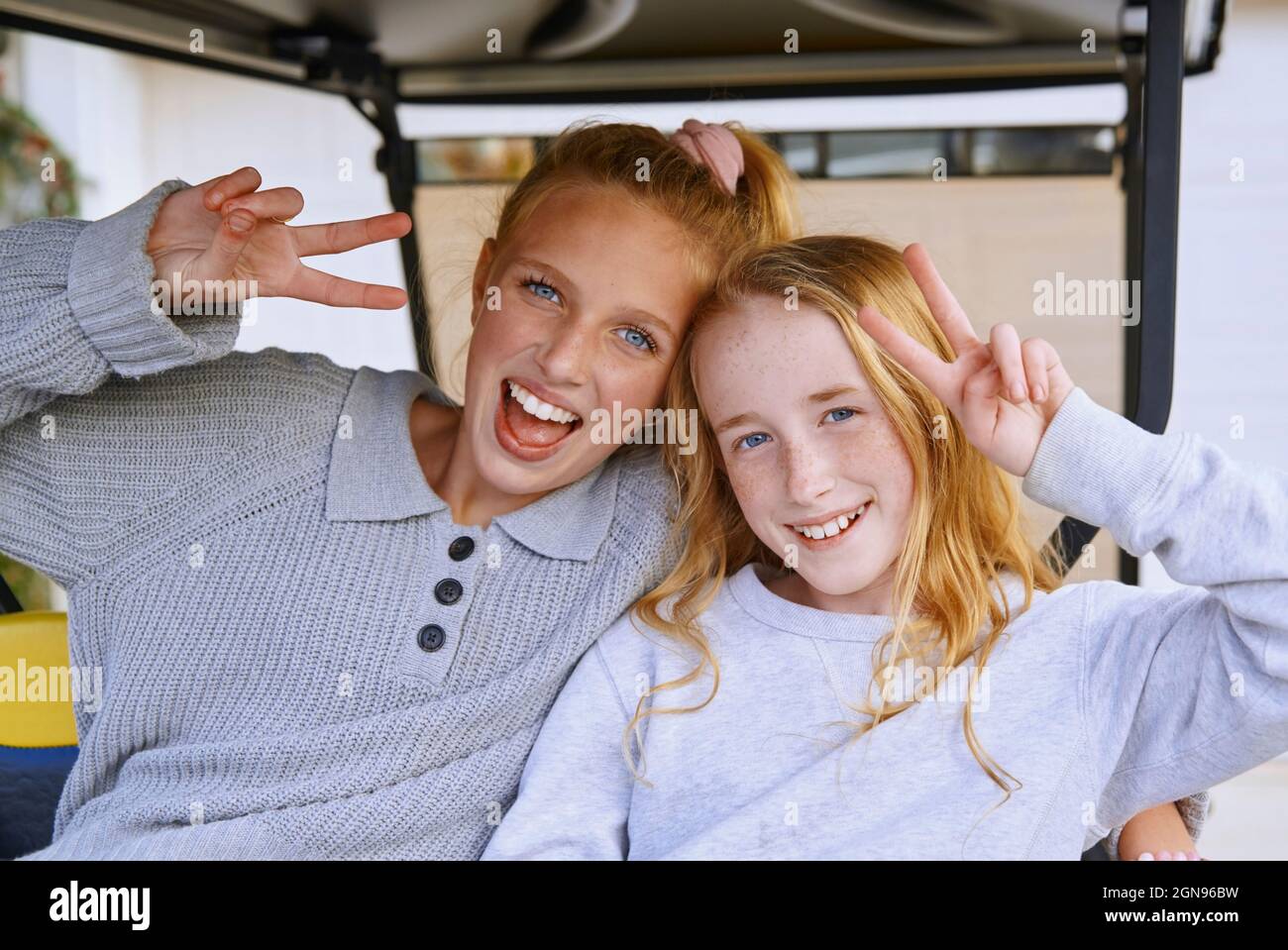 Happy girls gesturing peace sign while sitting in golf cart Stock Photo