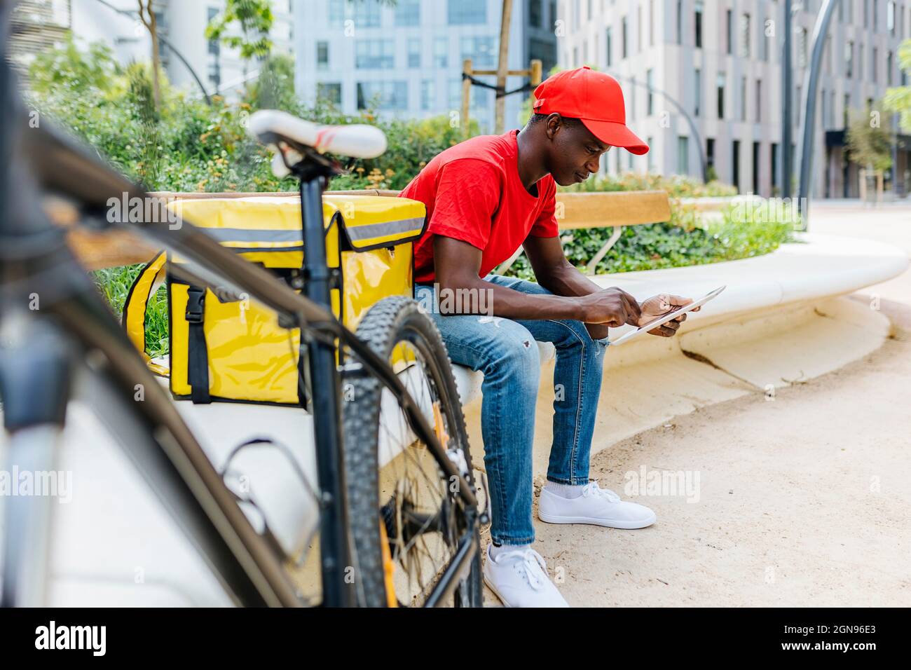 Young delivery man using digital tablet while sitting by package on bench Stock Photo