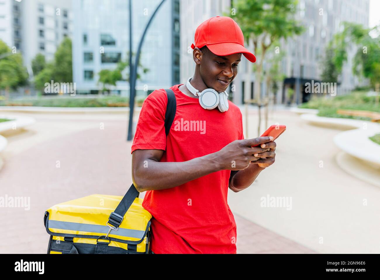 Delivery man wearing backpack text messaging through mobile phone Stock Photo