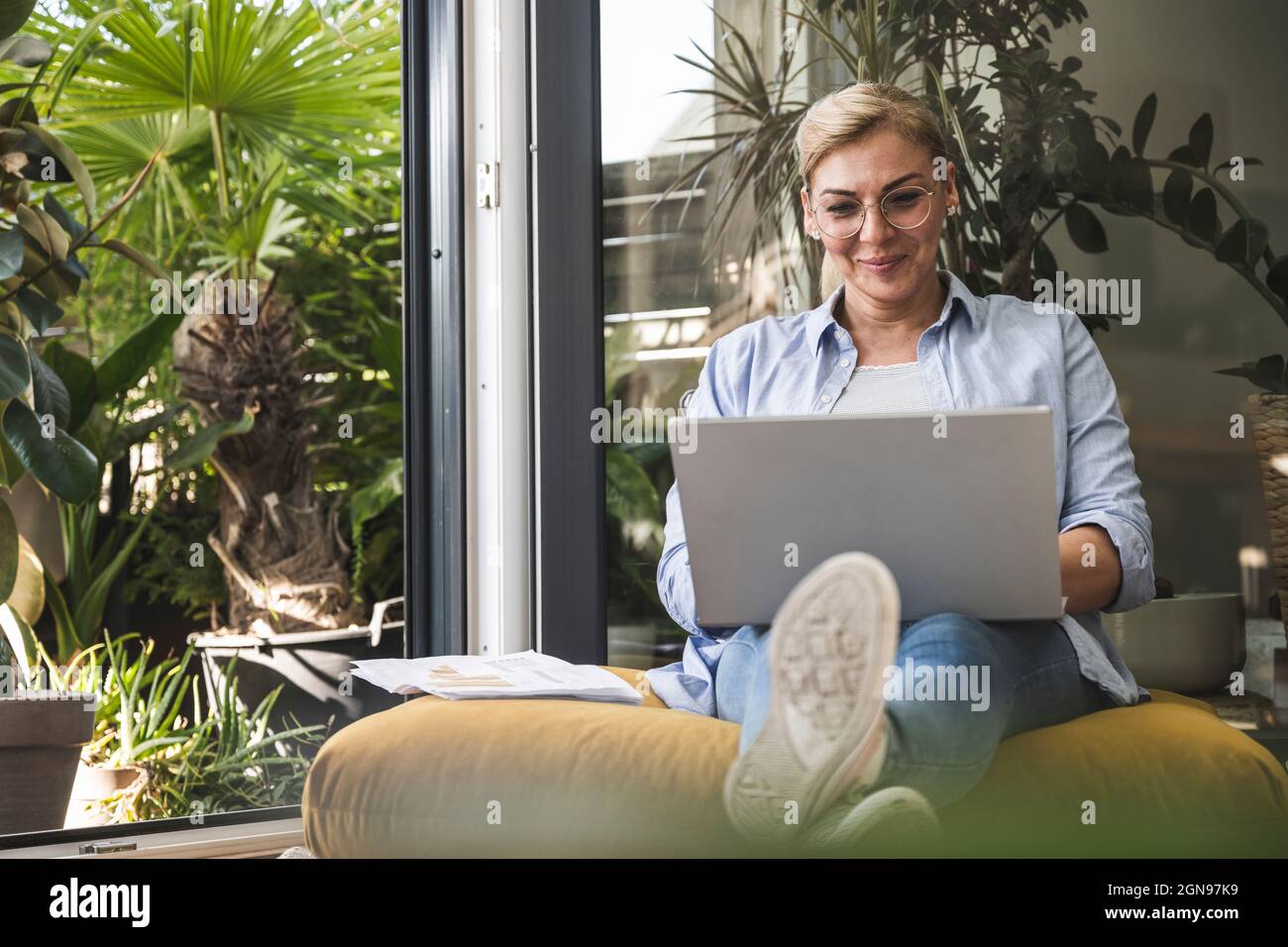 Smiling female freelancer using laptop while sitting by window Stock Photo