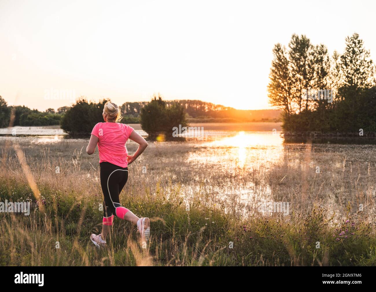 Woman exercising while running on grass during sunset Stock Photo