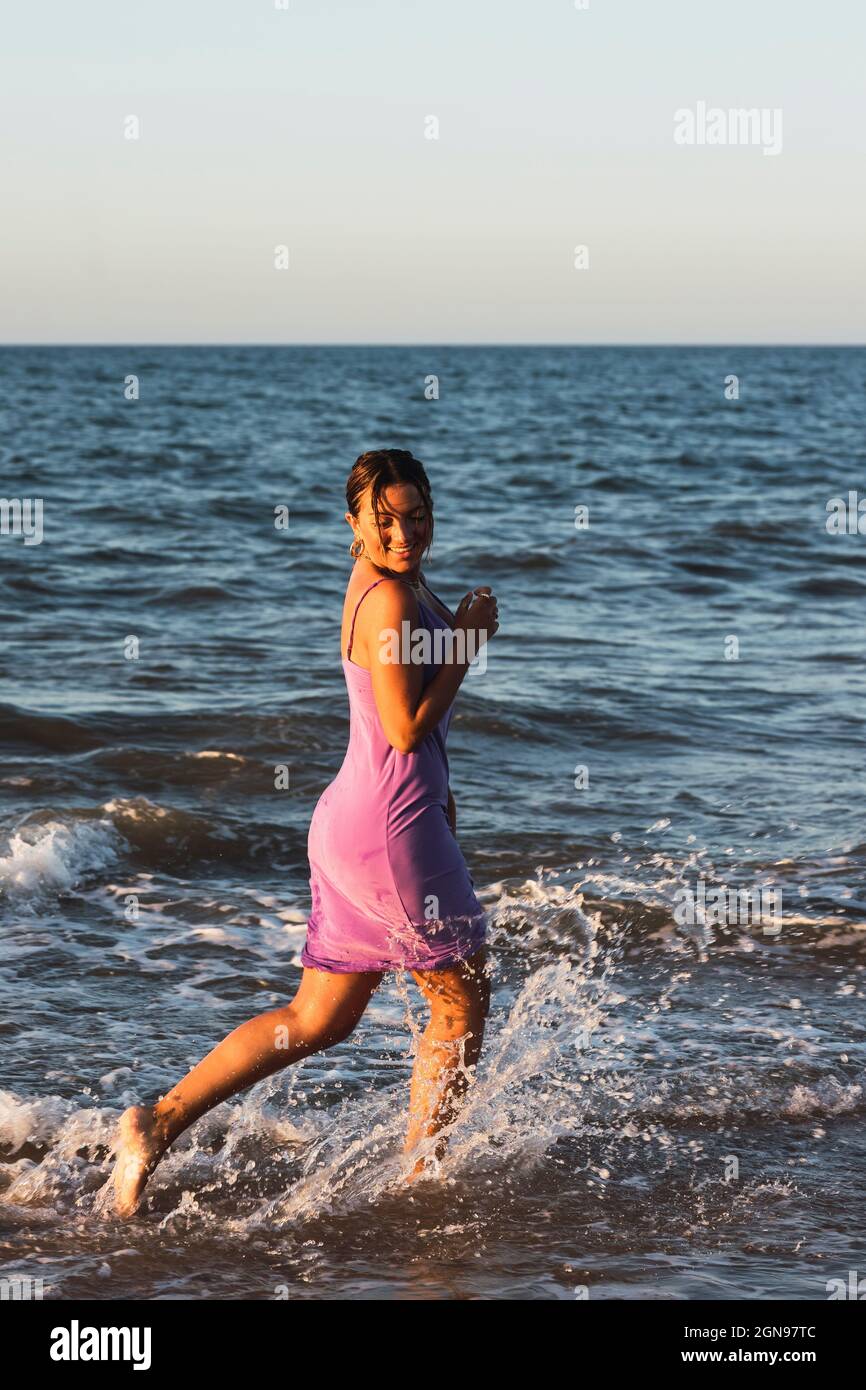 Playful woman splashing water while running on beach Stock Photo