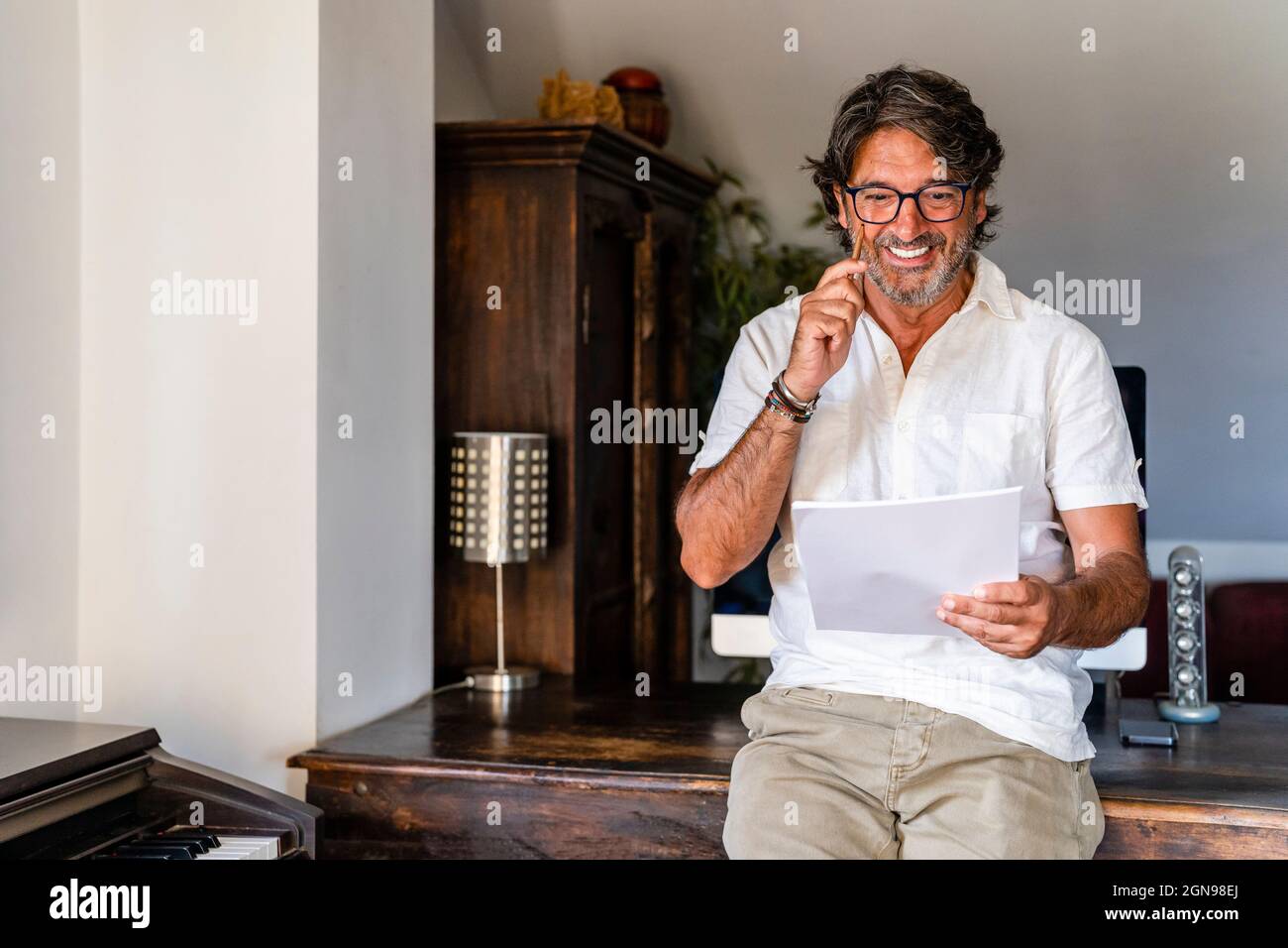 Smiling businessman checking document while leaning on desk at home office Stock Photo