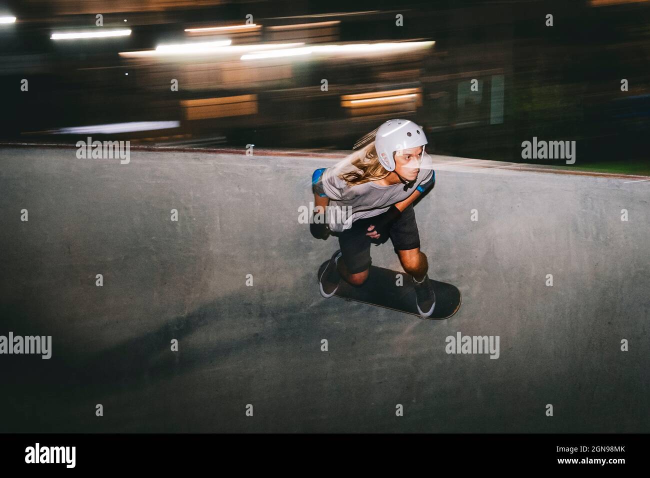 Man wearing helmet while skateboarding on sports ramp at night Stock