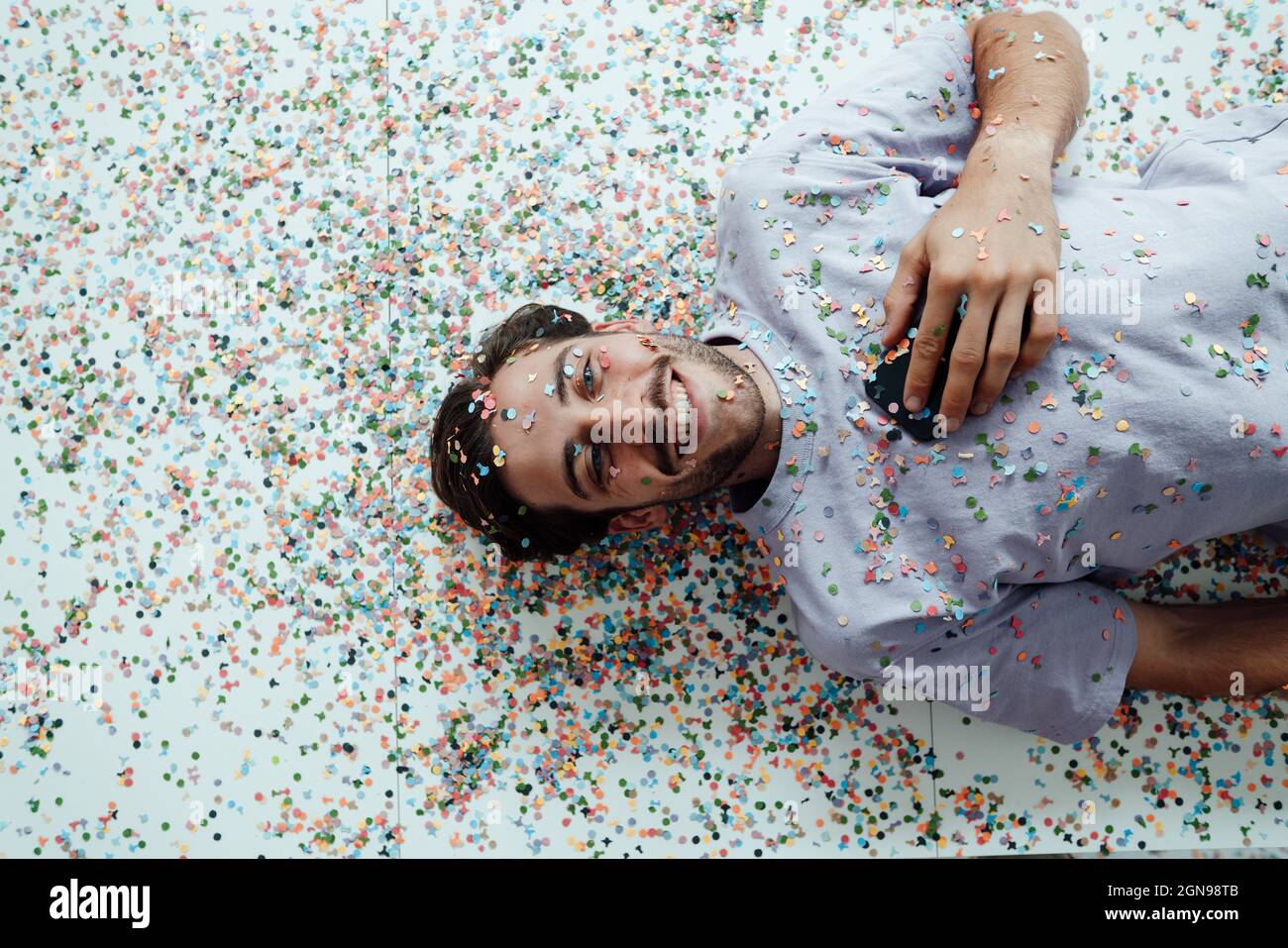 Smiling man lying with confetti on floor Stock Photo