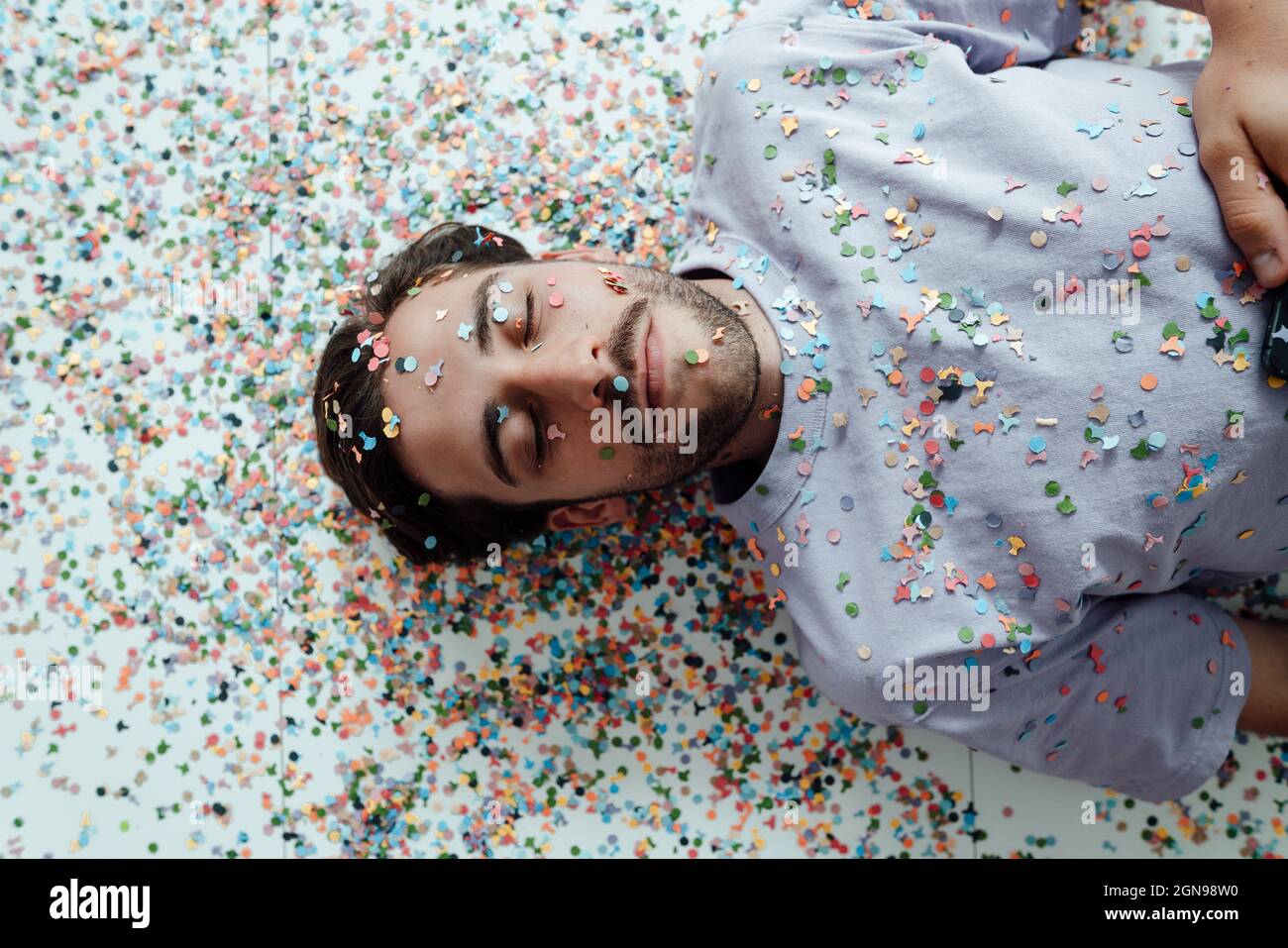 Man's face covered with confetti relaxing on floor Stock Photo