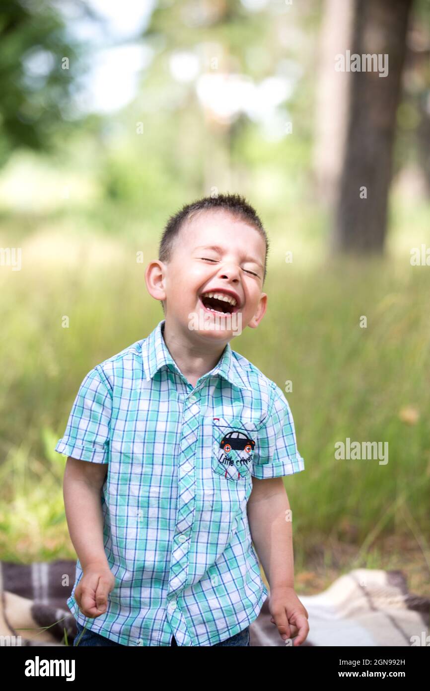 the boy is sitting on a blanket in the park and laughing merrily Stock Photo